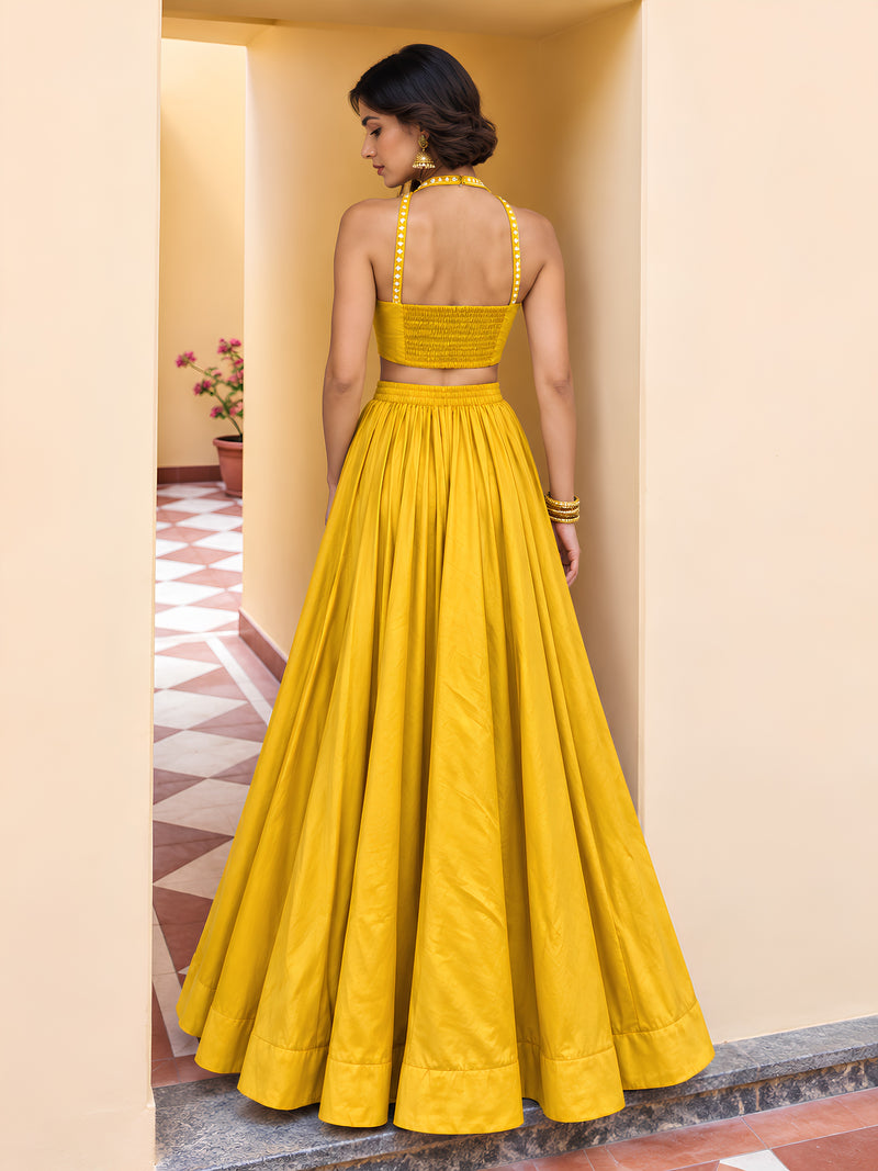Back view of yellow lehenga set showing smocked choli panel, halter straps and flowing full-length skirt