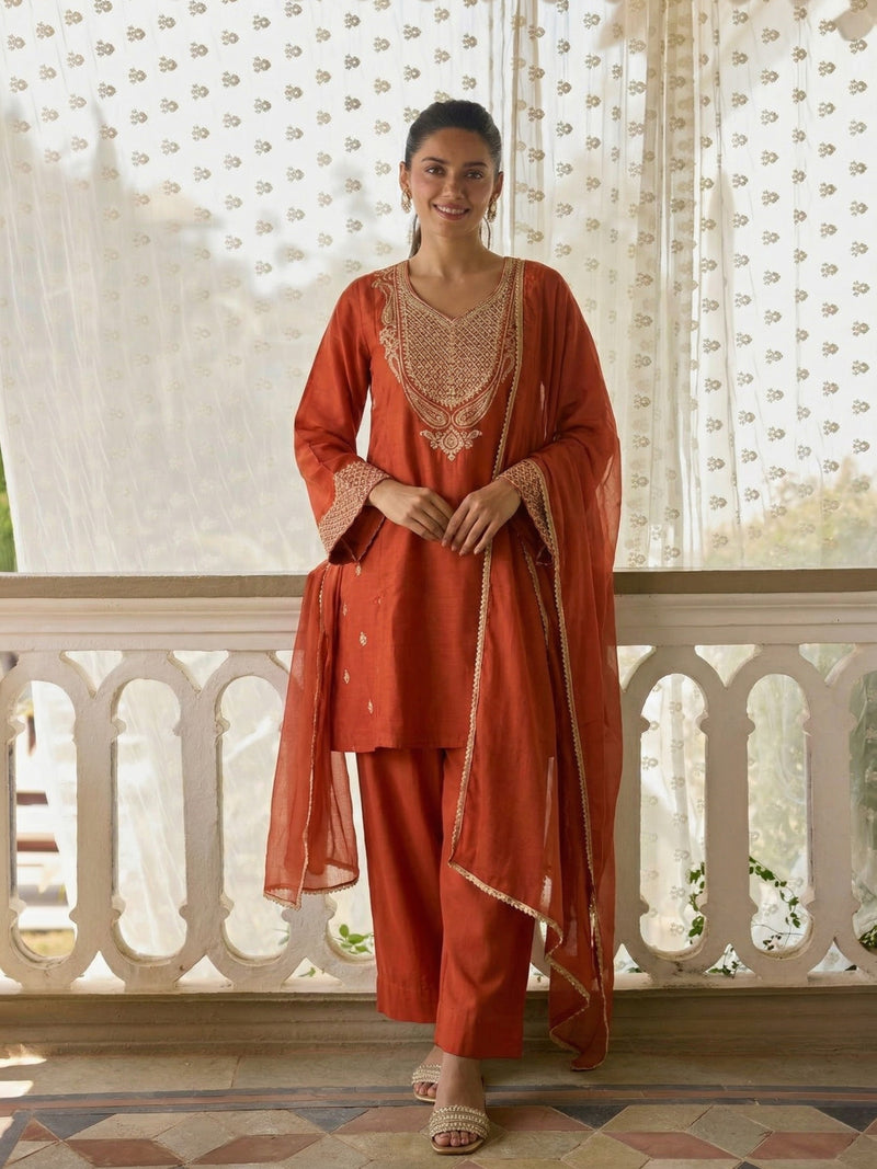 Woman wearing an orange traditional outfit with intricate embroidery in a decorative setting.