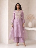 A woman models a lavender purple traditional Indian outfit consisting of a long kurta with gold embroidery, matching trousers, and a sheer matching dupatta, set against a minimalist beige wall with a decorative vase.