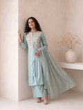 A woman models a light blue-green traditional Indian salwar kameez suit with beige embroidery on the chest, paired with matching trousers and a sheer dupatta, set against a minimalist beige wall background.