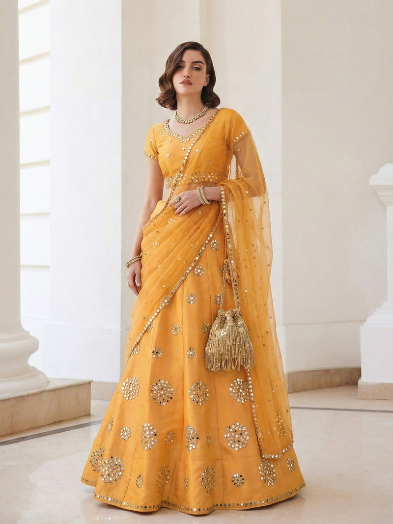 Woman in a yellow saree with gold embroidery standing in a bright room.