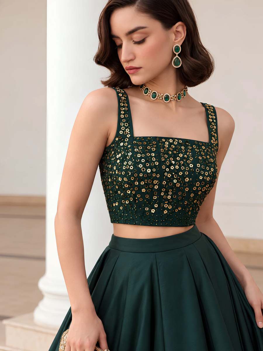 Close-up of the deep emerald green choli showing its square neckline, gold embellishment and shoulder straps