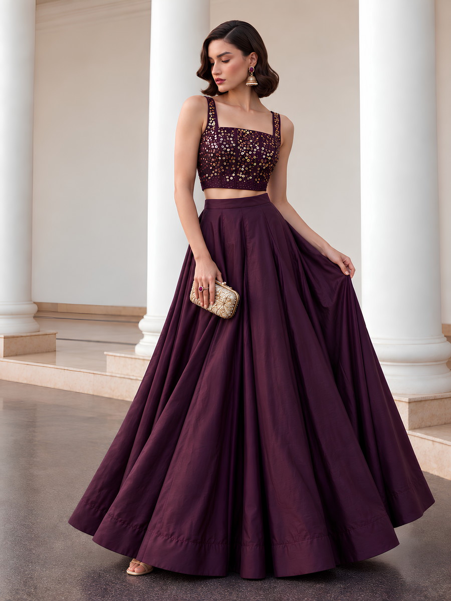 Front view of the Midnight Noir deep plum lehenga set styled with a gold clutch and gold-embellished choli